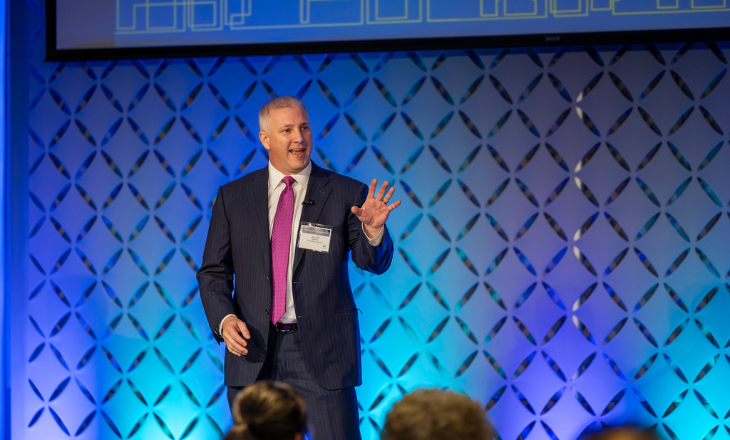 Man presenting at conference against bright blue background.