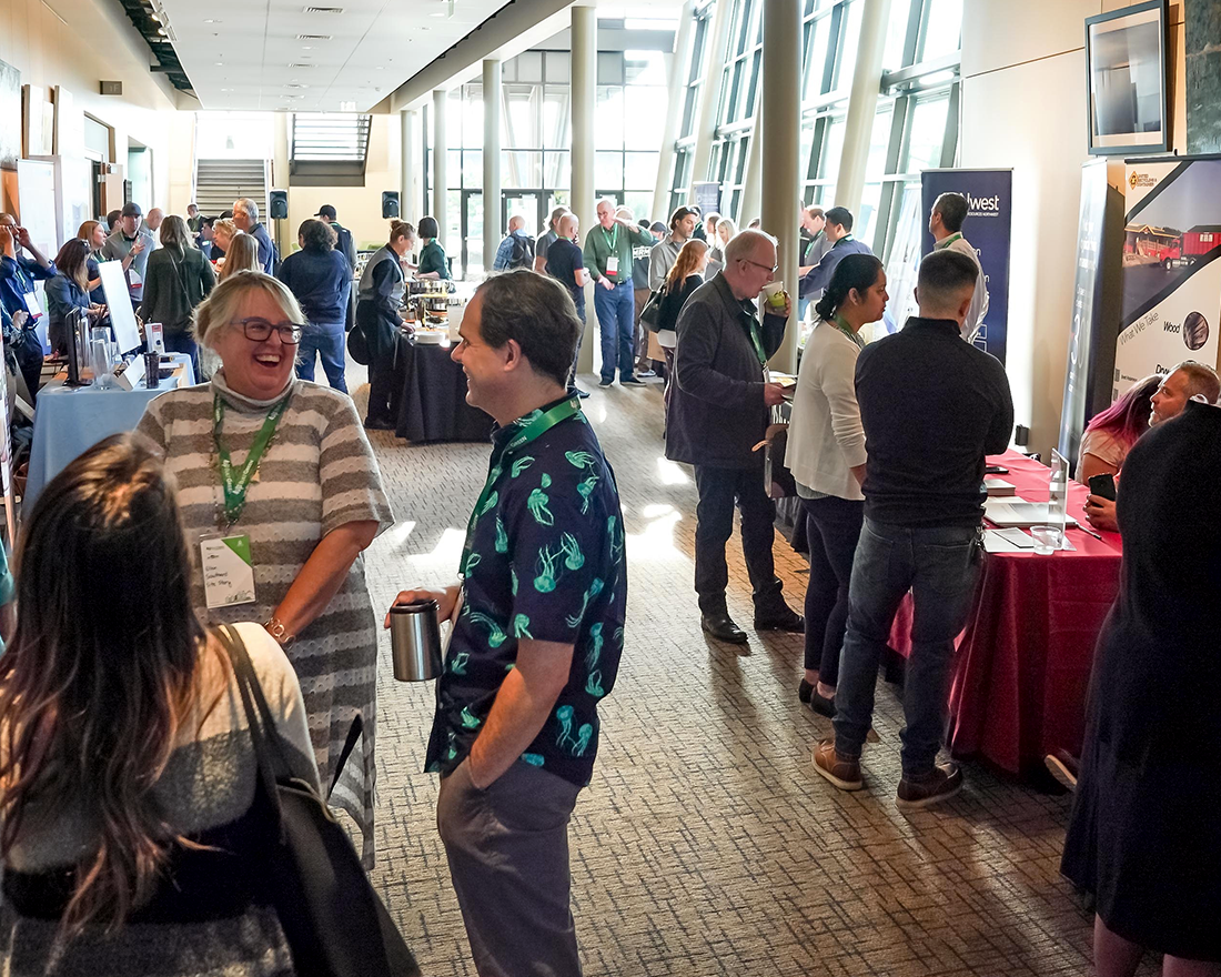 A crowd mingles in a conference hall lined with sponsor tables