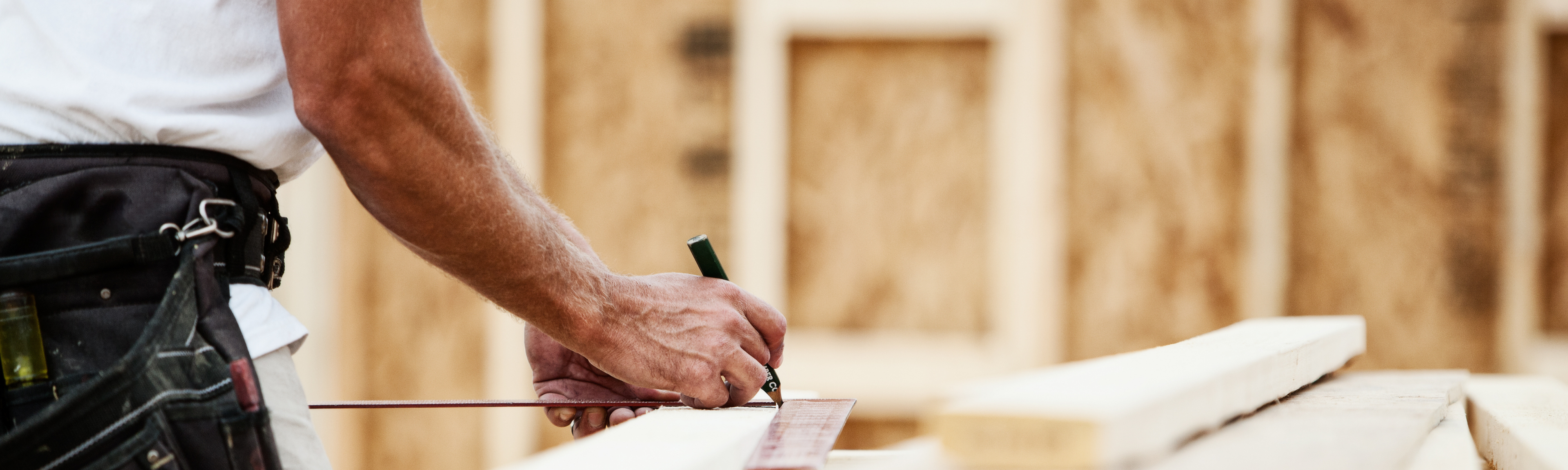 Hands using carpenter pencil to mark wood before cutting.