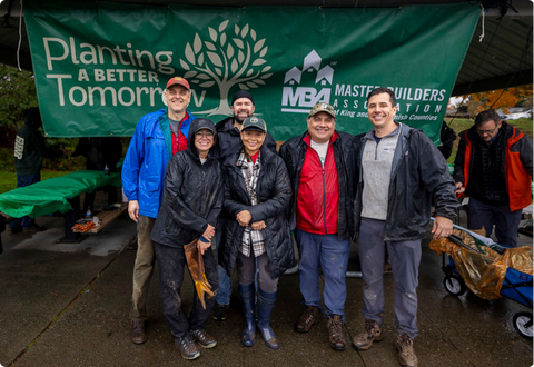 group poses in front of a planting a better tomorrow hanging sign outside in rain